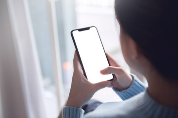 Mock up image of hand touching mobile smartphone with blank white screen in home interior, living room, copy space.