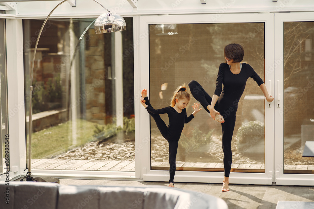 Girl is engaged in gymnastics. Family in a yoga studio. Kid in a black sportwear. - obrazy, fototapety, plakaty 