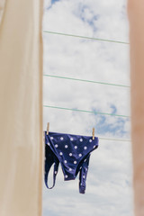 Wall Mural - Cute dots swimsuit hanging in a clothesline between bed sheets against cloudy sky. Beautiful and relaxing summer image.