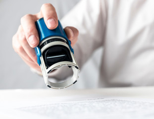 Poster - male hand of a businessman is preparing to put or putting a stamp on documents contract. Signing and stamping contract concept.