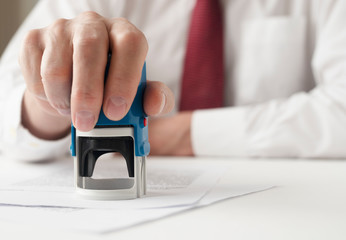 Poster - male hand of a businessman is putting a stamp on documents contract. Signing and stamping contract concept