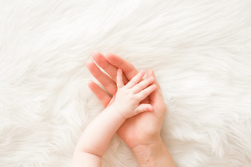 infant hand on mother palm on white fluffy fur background. lovely, emotional, sentimental moment. tr