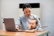 © imagenavi - Working woman while holding baby