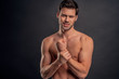 © Roman - Handsome young bearded man isolated. Cropped image of topless muscular man is standing on gray background. Man holding his wrist. Experiencing wrist pain.