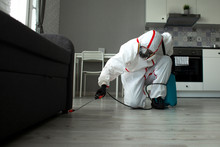 Pest Control. A Worker In A Protective Suit Cleans The Room From Cockroaches With A Spray Gun, The Sanitary Service Disinfects The Apartment With A Chemical Agent