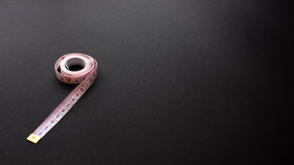 White tape measure on black texture background, office desk table from top view, copy space. 