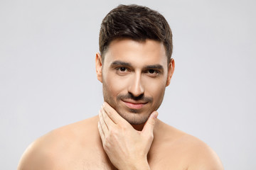 Handsome shirtless guy looking at camera, touching chin with fingers, feeling calm and confident, concept of skin care, isolated on gray background