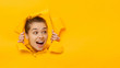 Horizontal banner of young female tearing paper and peeking out hole, curious about commercial offer on copy space on right, isolated on yellow background