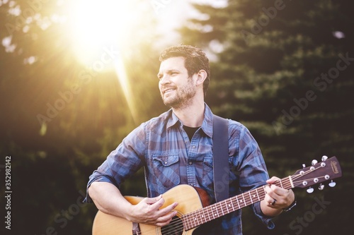 Cuadros en Lienzo Young male in a park holding a guitar and playing a song from the Christian hymn