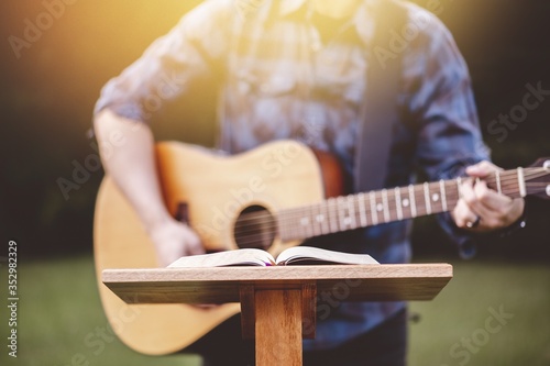 Fotomural Young male in a park holding a guitar and playing a song from the Christian hymn