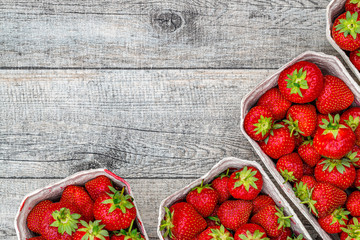 Wall Mural - Fresh German strawberries in carton paper boxes on wooden table, top view.  Red strawberry berrees harvesting concept