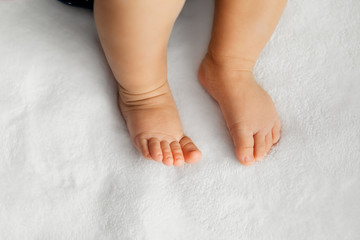 Wall Mural - Baby legs on soft white blanket as a background at natural light, infant feet in a selective focus