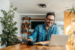 © bnenin - Happy entrepreneur at home office, looking at laptop and drinking cup of coffee, portrait.