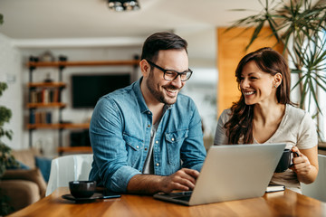 Portrait of a smiling couple at home, relaxing and using laptop.