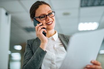 Wall Mural - Close-up portrait of a smiling woman talking on smart phone and looking at document.