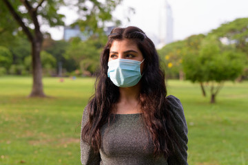 Sticker - Young Indian woman with mask thinking while relaxing at the park