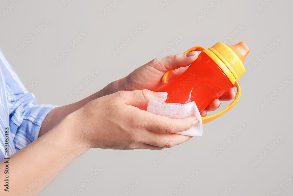 Woman disinfecting baby bottle on grey background