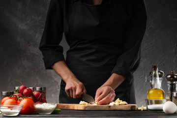 Wall Mural - Chef chopping garlic for cooking. Against the background of a gray wall, and vegetables. Cooking and recipe book.