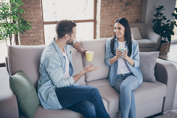 Poster - Portrait of positive loving married couple man woman have talk enjoy free time drink cappuccino cup sit couch in house indoors