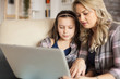 © DC Studio - Mother helping little daughter to type on laptop keyboard sitting on the ouch in living room.