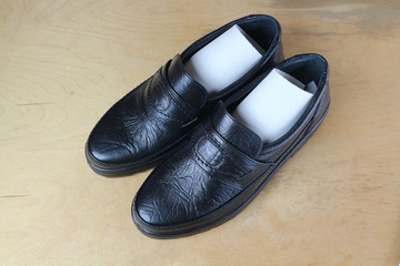 Black men's shoes on a wooden surface.