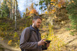 mężczyzna z brodą w lesie, na szlaku turystycznym, jesienią,  patrzy  na ekran telefonu 