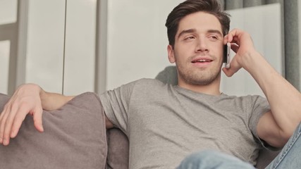 Poster - Young handsome pleased man talking by mobile phone indoors at home