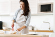 © Drobot Dean - Image of cheerful brunette woman preparing dough while cooking pie