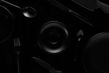 black empty plate in middle around black dishes on a black background