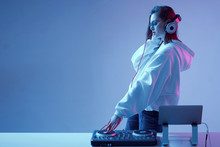 Cool Young Girl DJ Mixes Music On A Mixing Console And Laptop, In Stylish Clothes, Glasses On A Neon Background.