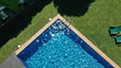 Aerial top down view of swimming pool with stairs and empty sun beds loungers on green grass. Private villa. Relaxing outdoor area.
