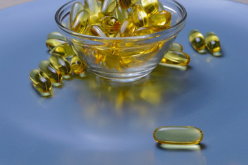 Omega-3 and Vitamin D fish oil capsules in a glass plate.