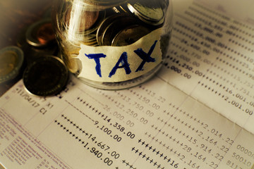 The glass jar full with the coins with TAX word on saving account passbook background. Financial and tax concept. Thai bath money in a jar.