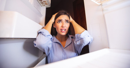 Desperate woman looking at empty fridge at home