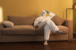 © LIGHTFIELD STUDIOS - Man in medical mask, decontamination suit and latex gloves sitting on couch at home