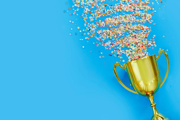 image of little gold cup , concept for winning or success. golden trophy cup and streamers on blue b
