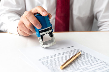 Poster - male hand of a businessman is preparing to put or putting a stamp on documents contract. Signing and stamping contract concept.