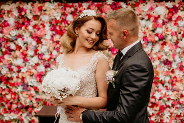 Wall Mural - beautiful wedding couple posing outdoor in front of flower wall