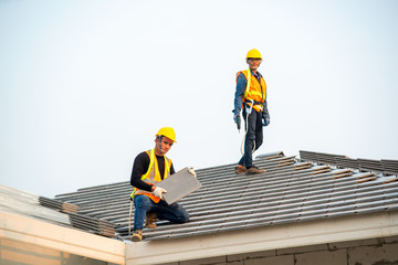 Poster - Roofer worker in special protective workwear and gloves installing new roof under construction residential building.