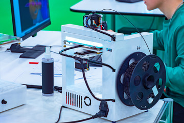 Poster - 3D printer next to a person. A man creates a 3D object. A printer for printing three-dimensional parts near a computer. Equipment for professional 3D printing. The press of volume objects.