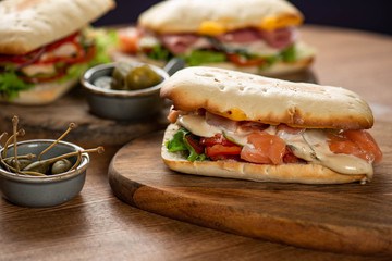 Wall Mural - panini or hot sandwiches with beef, ham, herbs and cheese, tomatoes and red pepper on a wooden cutting board