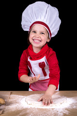 happy and smiling little girl making dough with cook's hat on black background