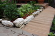  Walkways made of wood-plastic composite boards. A border made of natural stone and flower pots. Gardening and decoration of the house plot. Solar lights.