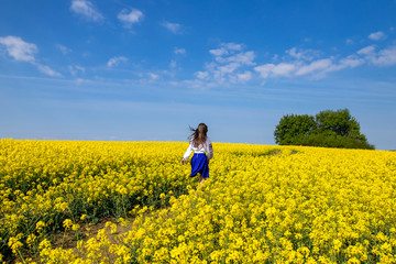 Wall Mural - young woman running in a field with yellow flowers, blue sky, space