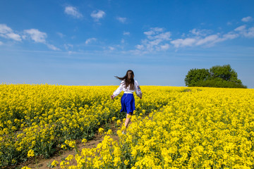 Wall Mural - young woman running in a field with yellow flowers, blue sky, space