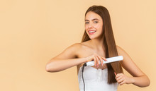 Hairstyle. Beautiful Smiling Woman Ironing Long Hair With Flat Iron. Happy Woman Straightening Hair With Straightener. Portrait Of Young Beautiful Girl Using Styler On Her Shining Hair