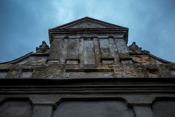 The wall of an ancient building resembling a Catholic church is decorated with statues against the blue sky.