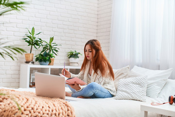 cute teen girl doing homework sitting on the bed at home. distance learning.