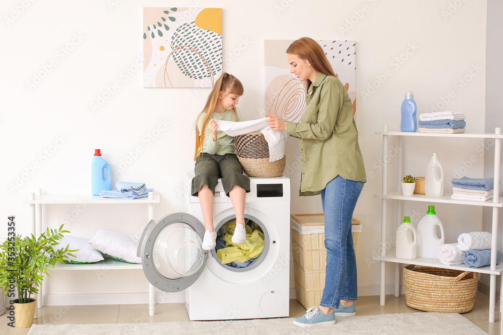 Woman and her cute little daughter doing laundry at home