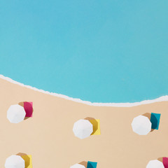 Colorful minimalistic sandy beach and sea made out of paper. Beach umbrellas and towels. Summer vacation background concept.
